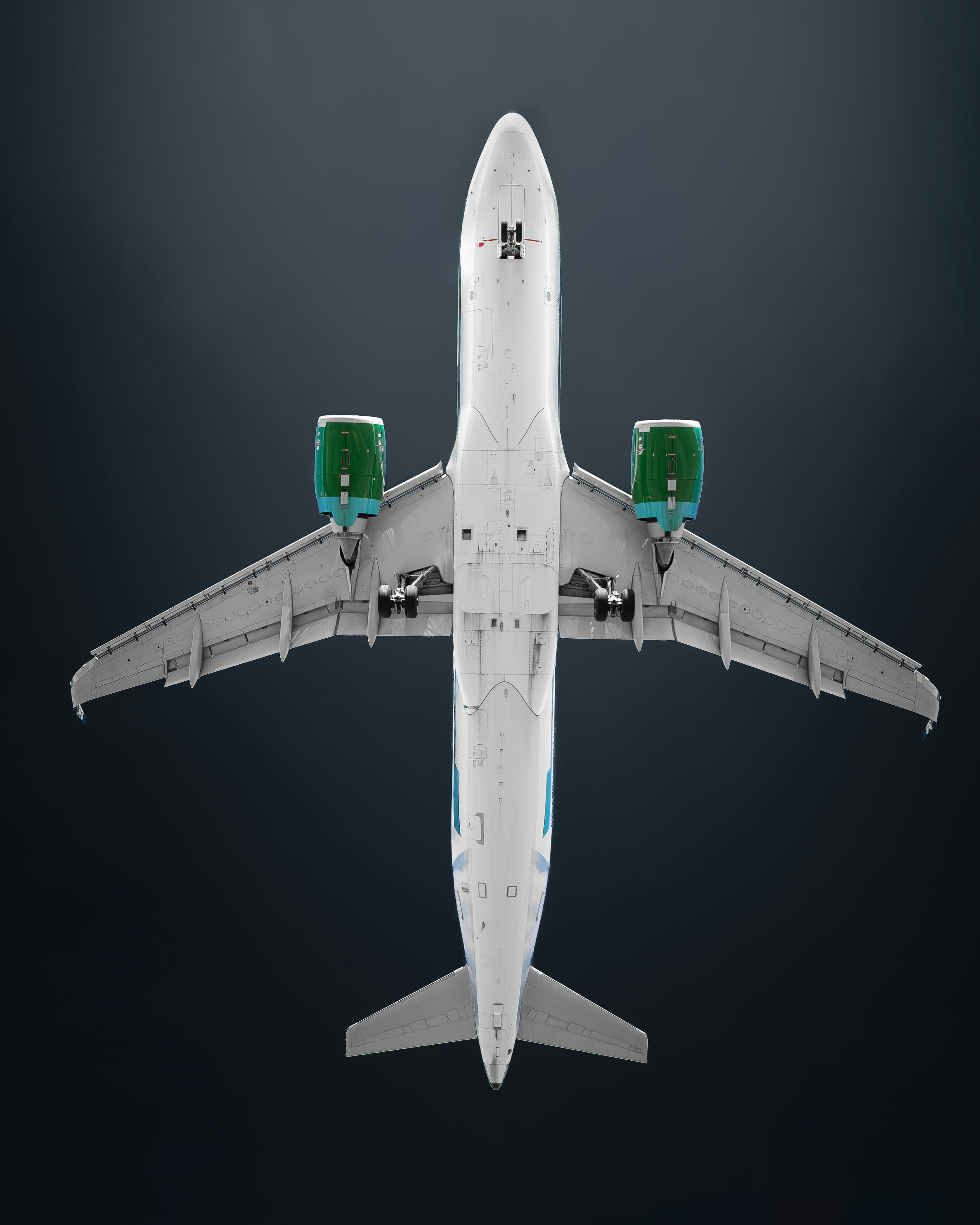 An airplane viewed from below against a dark background, highlighting its white fuselage and green engine covers.